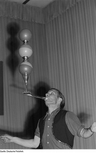 man balancing balls and glasses on a rod from his mouth